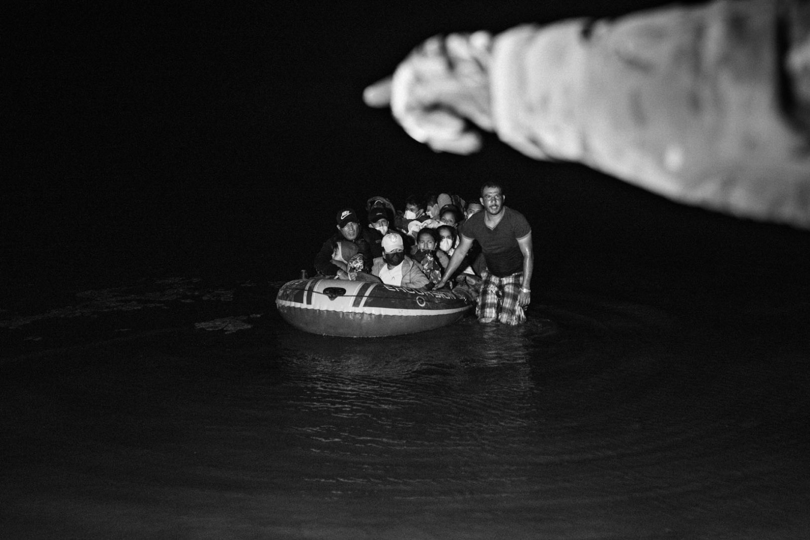 A man leads a group of migrants across the Rio Grande while an American soldier points to an easy docking point in Roma, Texas, on May 28, 2021.
The United States was essentially closed to asylum seekers for most of 2020, denying their claims with arguments based on Title 42, a U.S. statute that allows the expulsion of migrants from a country where a virus such as Covid-19 is present. 
In 2021, an unprecedented number of people seeking humanitarian protection arrived at the border, traveling across Latin America from Brasil, Venezuela, Ecuador, Haiti, Central America, and even African and Asian countries.
The photographer has worked in Roma between May and June 2021, using a light source to photograph the scenes of migrants guided by a boatman into the U.S. 
From the shore, gunshots on the other side of the border revealed a continuous war between cartels to control the migrant trade. People commented on having spent several days, or weeks, in isolated farms on the Mexican side waiting for the traffickers to move them at the Rio Grande River.
The boatman depicted in this picture gave his permission to be photographed. He said he was paid 20 dollars for each people on his dinghy.