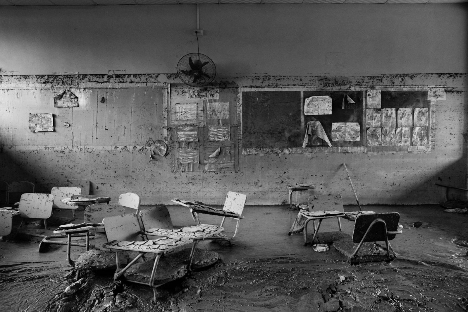 View inside a mud-covered classroom in Chamelecon, in San Pedro Sula, Honduras, on January 11, 2021. 
When hurricanes Eta and Iota hit Central America in November 2020, the Chamelecon neighborhood was one of the most affected areas of San Pedro Sula.
According to UNICEF, 1.772.033 children in Honduras were affected by the disaster. Access to regular education, already complicated by the pandemic, was impossible with destroyed schools. 
The entry to this conflictive area, controlled by local gangs, was granted by the support of a community leader, who, like many other people, migrated to the Northern Mexican border in mid-January. The photographer met him again in Ciudad Juarez, in Mexico, months after, when he commented he was living with his girlfriend and a step-daughter. He had found a source of income but refused to specify his occupation. 
His dead body, with signs of tortures and a coup de grace, was found in a street of Ciudad Juarez on September 15, covered by a blanket, a symbol used by the Mexican cartels to announce executions.