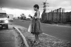 A young girl looks at the empty plastic glass she recollects the alms in, along a street of the capital city Bogotà, on October 31, 2018.
In October and November 2018, the photographer documented the living conditions of Venezuelan refugees and migrants in an area close to the capital city's bus terminal, where approximately three hundred people were living in makeshift tents.
On the day of this photograph, compassionate Colombians had come to the settlement to cheer the children up by distributing Halloween dresses. A young girl was begging for money and exchanging candies for coins with the drivers passing by the street. Like other children, she ran to receive a dress, quickly wore it, and walked toward the traffic island again.
In November, Colombian authorities dismantled the camp, forcing people to continue their journey to other Colombian cities or the southern border between Colombia and Ecuador. Others resettled in an official humanitarian settlement, also dismantled a month later. The photographer was, by the time, well known by the families in the camp, who granted their consent to work. A young girl looks at the empty plastic glass she recollects the alms in, along a street of the capital city Bogotà, on October 31, 2018.
In October and November 2018, the photographer documented the living conditions of Venezuelan refugees and migrants in an area close to the capital city's bus terminal, where approximately three hundred people were living in makeshift tents.
On the day of this photograph, compassionate Colombians had come to the settlement to cheer the children up by distributing Halloween dresses. A young girl was begging for money and exchanging candies for coins with the drivers passing by the street. Like other children, she ran to receive a dress, quickly wore it, and walked toward the traffic island again.
In November, Colombian authorities dismantled the camp, forcing people to continue their journey to other Colombian cities or the southern border between Colombia and Ecuador. Others resettled in an official humanitarian settlement, also dismantled a month later. The photographer was, by the time, well known by the families in the camp, who granted their consent to work.