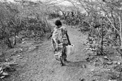 Adriana Uriana returns home with a bucket of water from a well her community dig to get water.